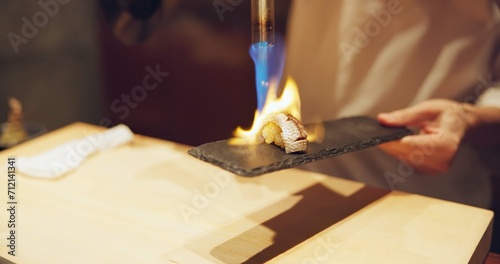 Hands, fire and cooking sushi with chef in restaurant for traditional Japanese food or cuisine closeup. Kitchen, flame for seafood preparation and person working with gourmet meal recipe ingredients photo