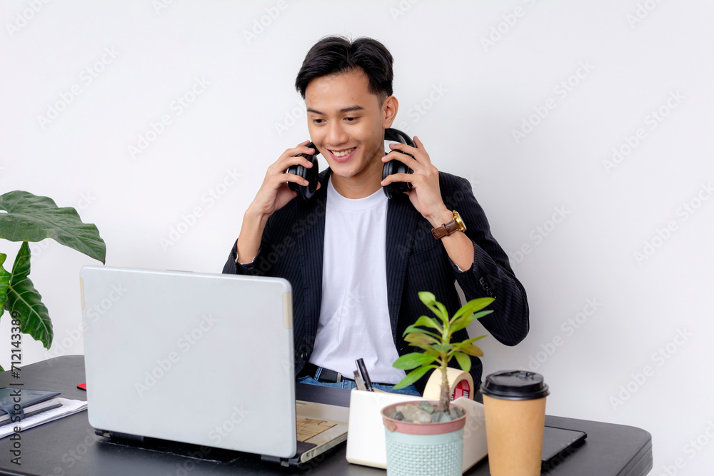 Smiling young adult balancing two phone calls while working on his laptop in a modern home office setting. Smiling young adult balancing two phone calls while working on his laptop in a modern home office setting.
