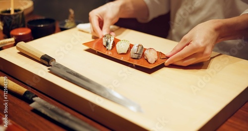Hands, food and chef serving sushi in restaurant for traditional Japanese cuisine or dish closeup. Kitchen, cooking or seafood preparation and person working on table with gourmet meal ingredients