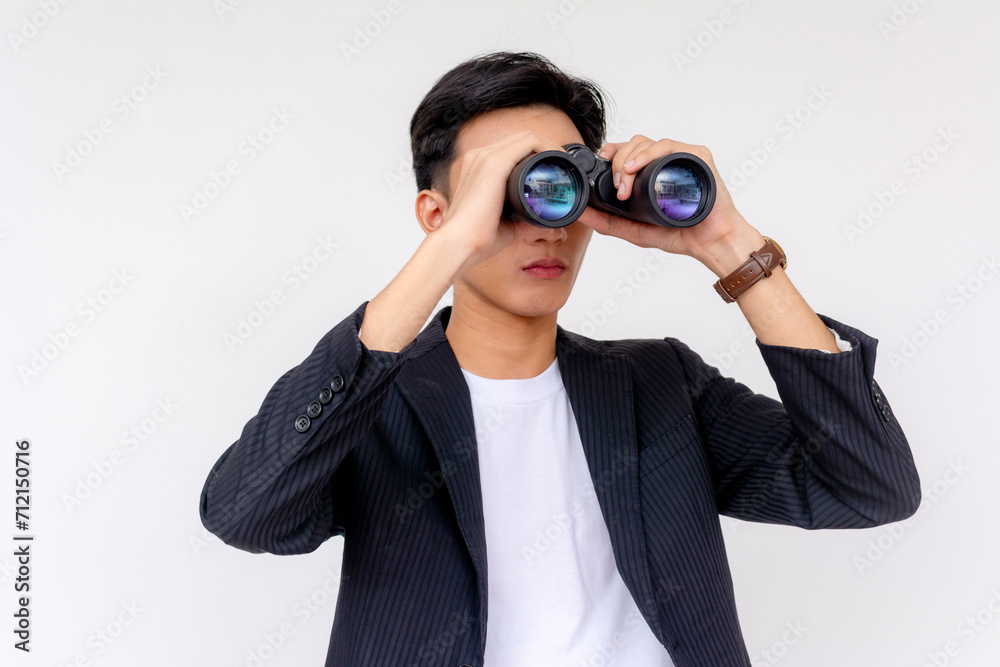 Focused young adult male in a smart suit peering through binoculars against a clean white backdrop. Focused young adult male in a smart suit peering through binoculars against a clean white backdrop.