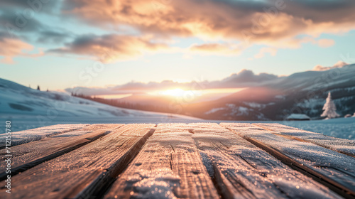 The empty wooden table top with snow and frost for your decoration of product or text and landscape of winter mountains with small rural home and sunset time