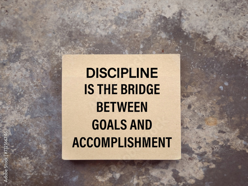 Motivational and inspirational wording. DISCIPLINE IS THE BRIDGE BETWEEN GOALS AND ACCOMPLISHMENT written on a notepad. With blurred style background. © Coompia77