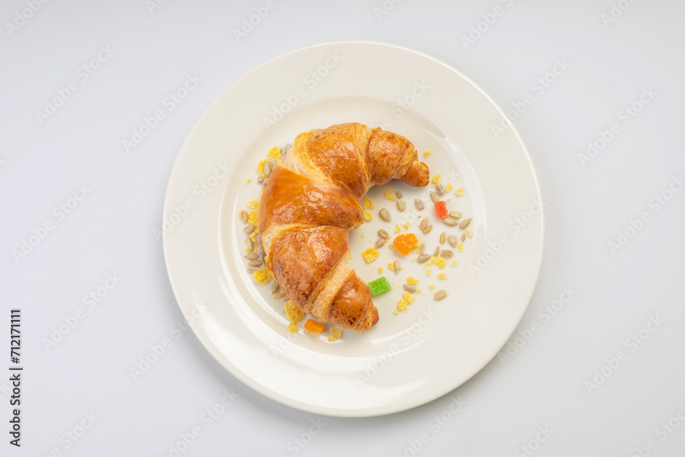 Breakfast. Croissant, seeds and dried fruits on a white plate and a white background Breakfast. Croissant, seeds and dried fruits on a white plate and a white background