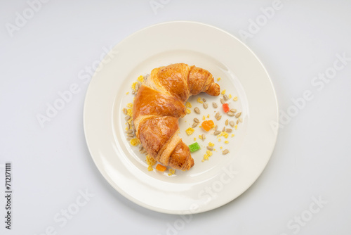 Breakfast. Croissant, seeds and dried fruits on a white plate and a white background