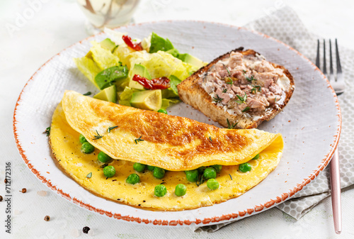 Omelette with green peas and toast with cod liver on white plate.  Frittata - italian omelet.