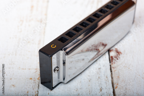 A metal harmonica with ten holes, a wind instrument, photographed on a wooden surface.