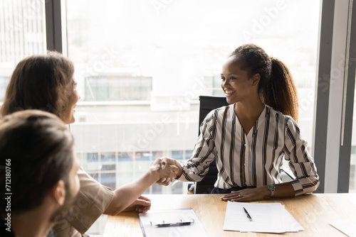 Happy confident African American businesswoman giving handshake to manager, reaching successful agreement, discussing cooperation, business partnership, contract on group meeting
