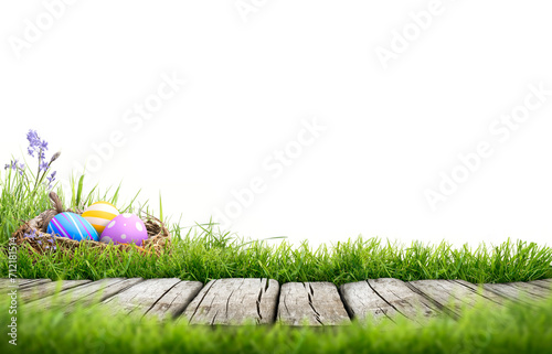 Obraz na płótnie A template with three painted easter eggs in a birds nest celebrating a Happy Easter with a wooden bench to place products on with green grass and transparent background w salonie
