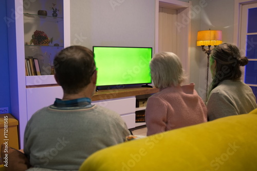Family watching TV. Green screen. Grandmother, her son and grandson are sitting on the couch at home and watching TV. In front of them is a green screen TV. 