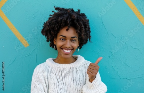 ctp afroamerican young woman in white sweater with thumbs up while pointing to right photo