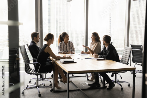 Diverse business partners meeting on serious conversation, talking at large table in modern office space with large urban window, discussing partnership, investment photo