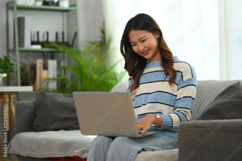 Smiling young woman relaxing on couch at home and using laptop. People and technology concept Smiling young woman relaxing on couch at home and using laptop. People and technology concept