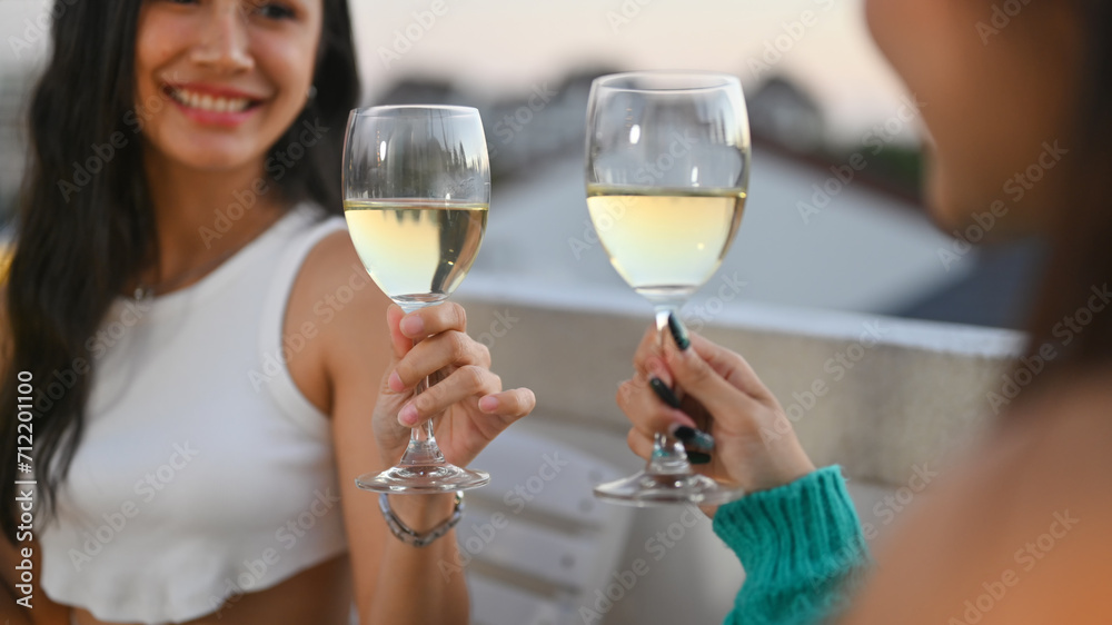 Cheerful Asian female friends toasting white wine celebrating together at rooftop dinner party