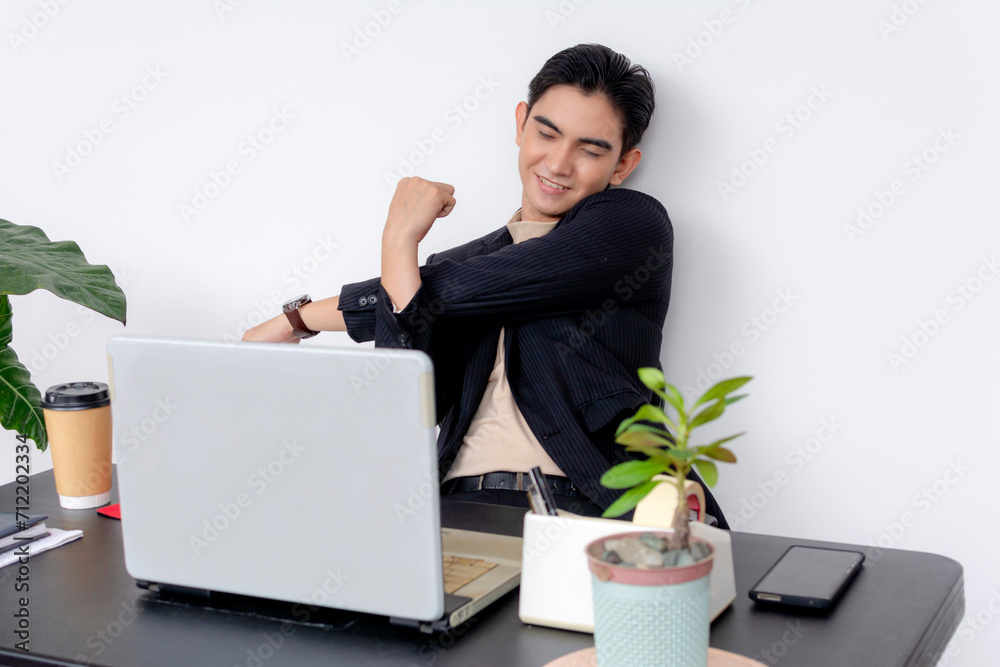 A relaxed Asian man smiling and stretching at his desk with laptop after a long day, exuding job satisfaction and casual professionalism. A relaxed Asian man smiling and stretching at his desk with laptop after a long day, exuding job satisfaction and casual professionalism.