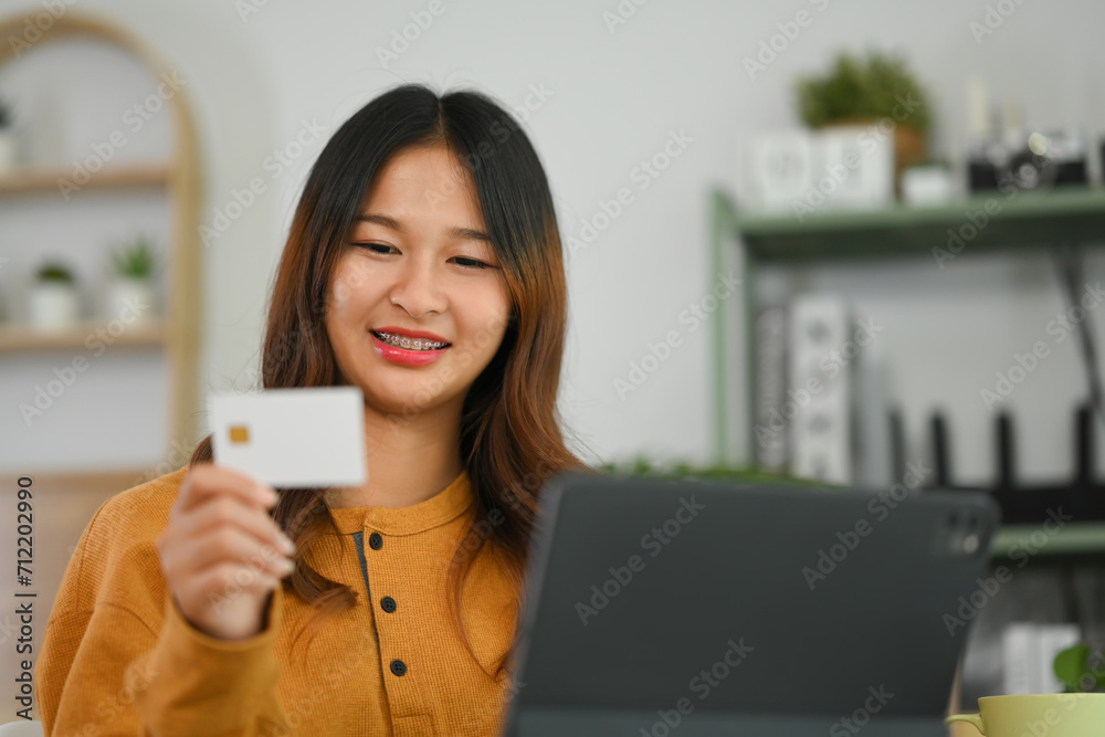 Satisfied young woman holding credit card and using laptop, making transaction or shopping online Satisfied young woman holding credit card and using laptop, making transaction or shopping online