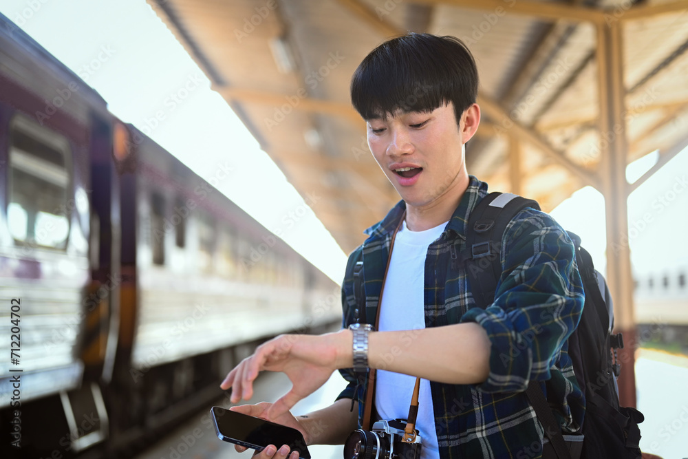 Male traveler with backpack checking time while waiting for train at platform. Male traveler with backpack checking time while waiting for train at platform.