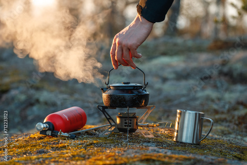 A man brews delicious tea in a kettle on a gasoline burner in the autumn forest.