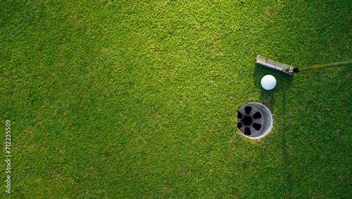 Top view of a golf ball with putter on green course at hole.