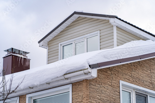 Corner of house with roof made of red metal tiles, chimney and gutter covered with thick layer of snow in winter. Metal Downpipe system, Guttering System, External downpipes and drainage pipes