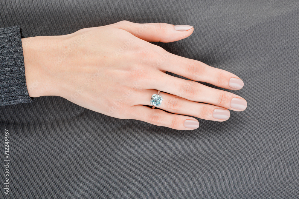 Beautiful female hand with gold ring with diamonds and aquamarine on gray background