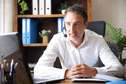 Photos Smiling man doing video conference with headphones in an office