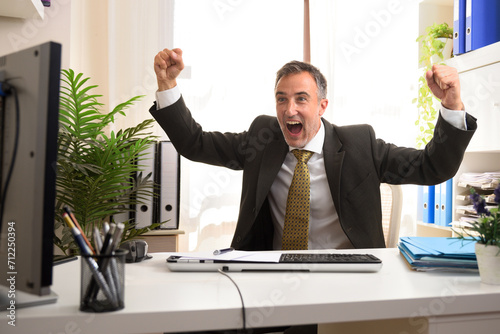 Businessman in office with fists raised looking at the monitor