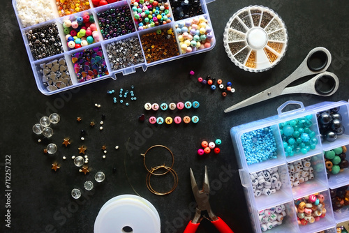 Colorful beads and various jewelry making supplies on dark background. Letter beads spelling JEWELRY MAKING. Top view. photo