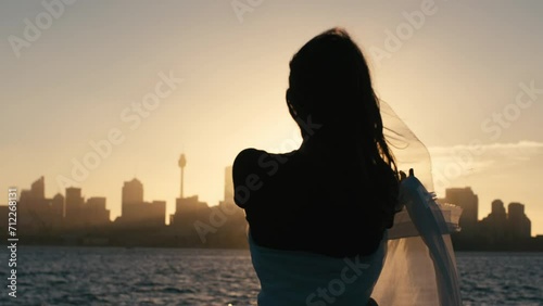 Silhouette of woman with white veil stands looking at the sunset over the city photo