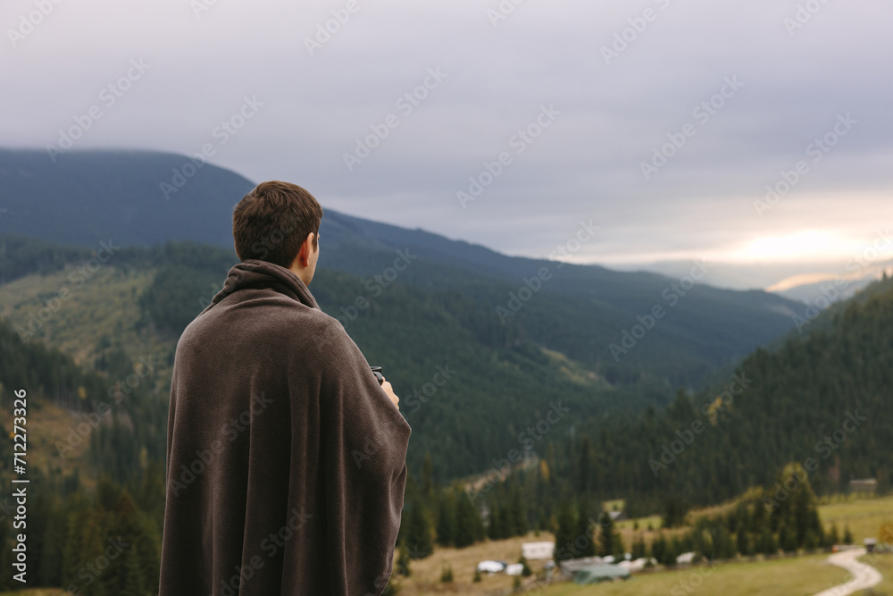 A young entrepreneur relaxes and meditates with a cup of tea in hand, watching a sunset on a mountain in the Carpathians