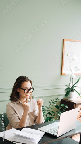 Victory and Joy. Smiling Woman Gesturing in Successful Laptop Video Chat. Triumphant Video Call. Joyful Woman in Glasses Beams as She Communicates on Laptop, Signaling Victory and Success.