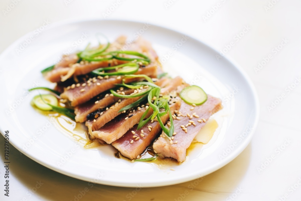 sliced tuna steak with green onions and sesame oil on white plate sliced tuna steak with green onions and sesame oil on white plate