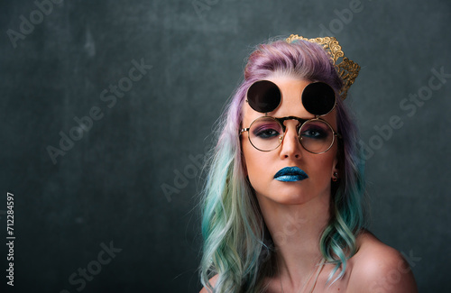 Woman With Blue and Green Hair Wearing Glasses. Portrait of a woman with blue and green hair, wearing glasses, in front of a neutral background.