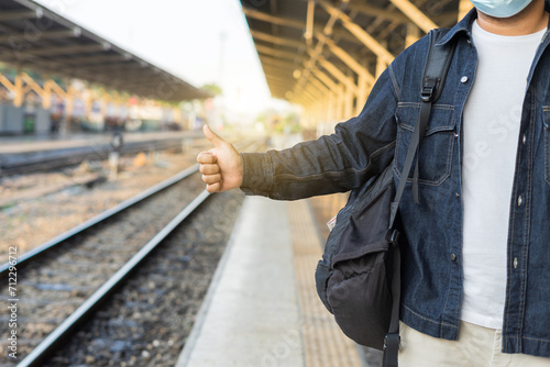 Young asian man traveler backpack in the train station. Backpacker male wear hat and denim jacket at the railway. Travel concept. The concept of a man traveling alone.