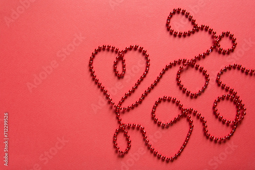 Heart shape with red ribbon made of beads on red background. Valentines day concept, empty card mockup 