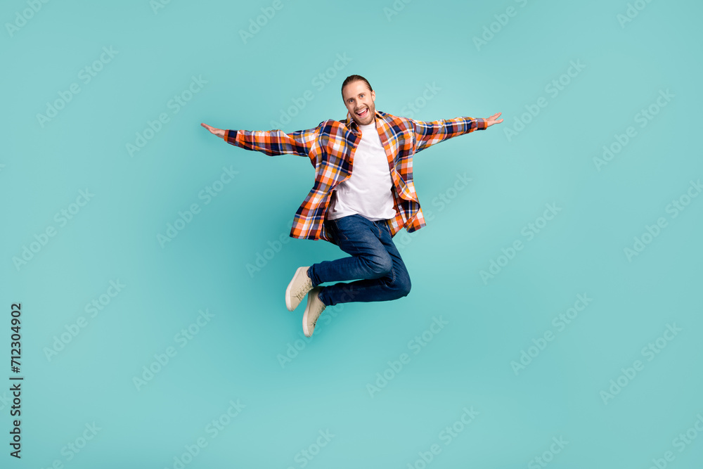 Full length photo of overjoyed man wear flannel shirt denim trousers flying hold hands like wings isolated on turquoise color background
