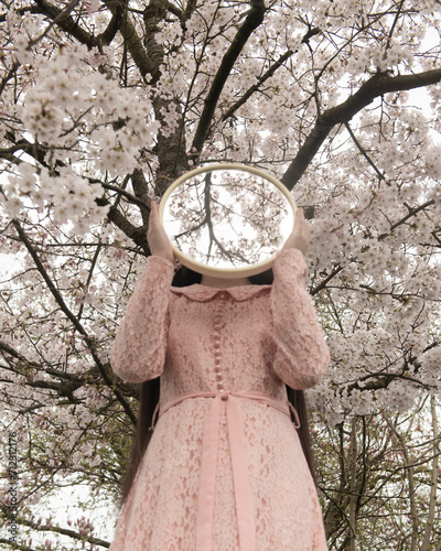 woman holding round mirror near blooming cherry blossom tree in spring