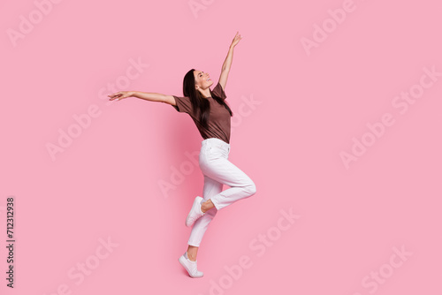 Full body profile portrait of overjoyed pretty lady raise hands enjoy dancing empty space isolated on pink color background