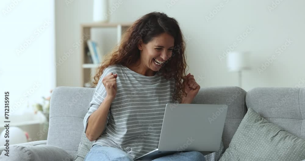 Young Latin woman celebrating online project success, typing on laptop at home, sitting on couch, getting happy, excited, making winner hand gesture at computer, shouting yes, smiling, laughing Young Latin woman celebrating online project success, typing on laptop at home, sitting on couch, getting happy, excited, making winner hand gesture at computer, shouting yes, smiling, laughing