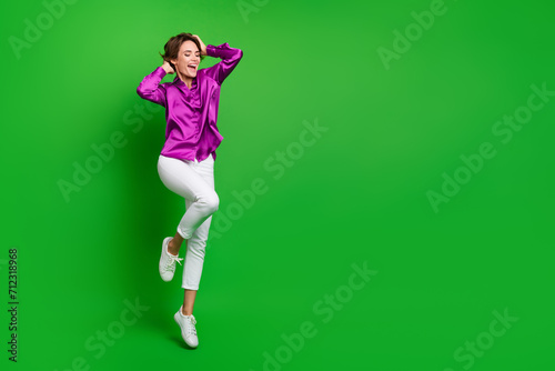 Full size portrait of stunning cheerful girl jumping hands touch bob hairstyle empty space isolated on green color background © deagreez