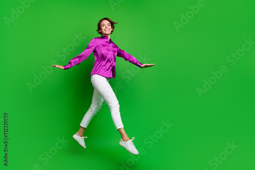 Full size profile photo of pretty energetic elegant girl jump run empty space isolated on green color background
