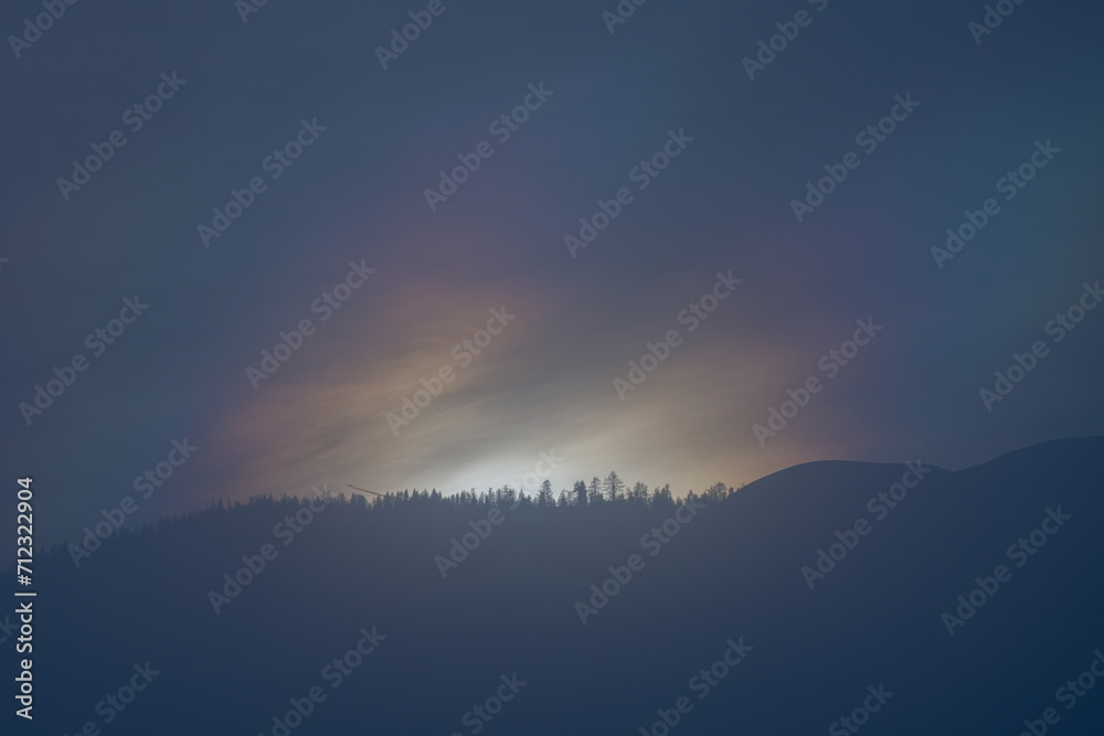 mystical sunrise over the mountains with a colorful light, fog and tree silhouettes