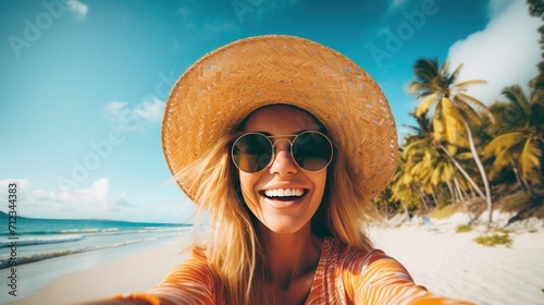 Happy young woman in straw hat and sunglasses takes a selfie on the beach against the backdrop of palm trees