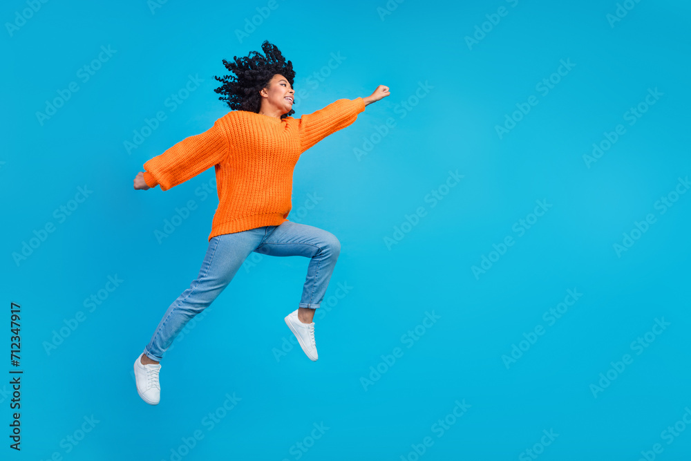 Full body photo of attractive young woman jump run have fun hurry dressed stylish knitted orange clothes isolated on blue color background