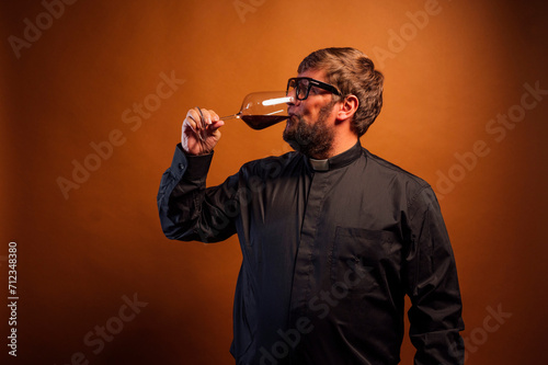 Portrait of a priest with crucifix and sunglasses drinking wine.