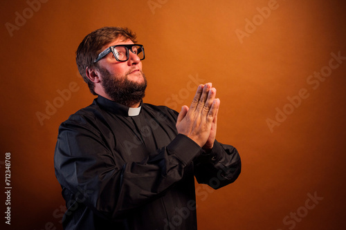 Portrait of a priest with crucifix and black shirt praying.