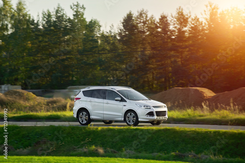 A subcompact SUV car explores the scenic countryside with a stunning sunset and alpine mountains in the background.