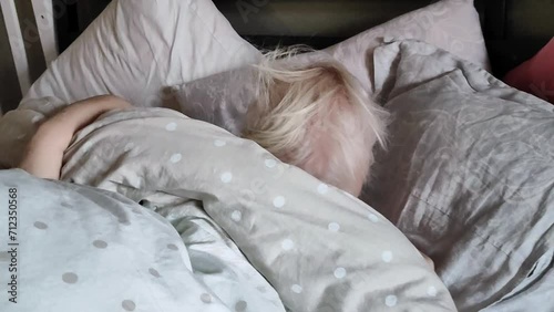 A little girl under two years old, sleepy in bed, crawls out from under the blanket and covers herself with the blanket again. Daytime sleep for babies. photo
