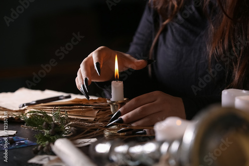 Witch with burning candle at dark table, closeup photo