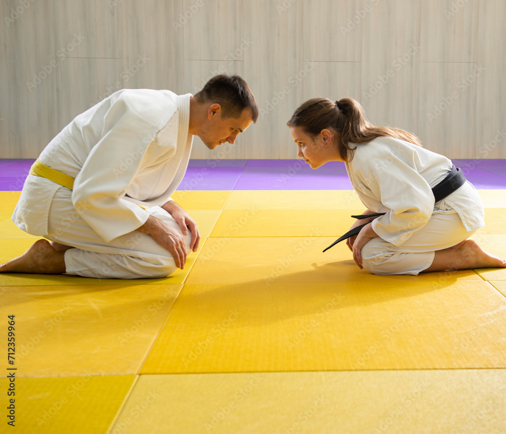 Yellow belt judo man in white judogi and young black belt judo girl in white judogi