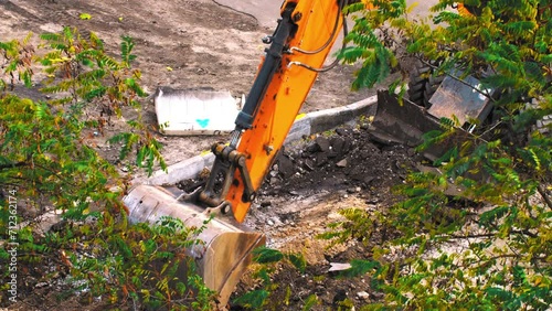 Excavator transferring a ground with a heavy bucket. Excavator at work. Tractor with a bucket on a construction site. A construction machine is making a road. Excavator bucket breaks the road asphalt